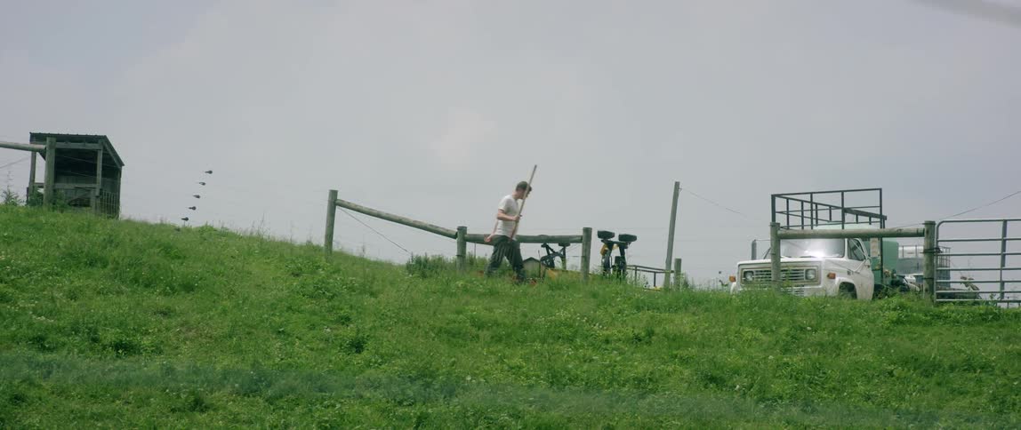 A man walks down a grassy hill with a pitchfork