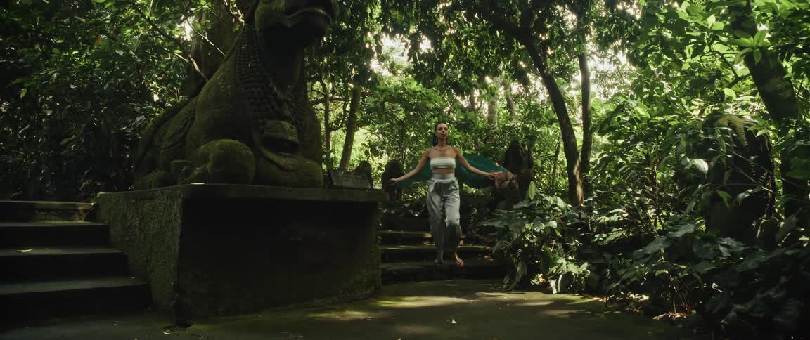 A graceful woman with a flowing scarf explores the ancient, moss-covered steps of a temple ruin deep within a lush green jungle