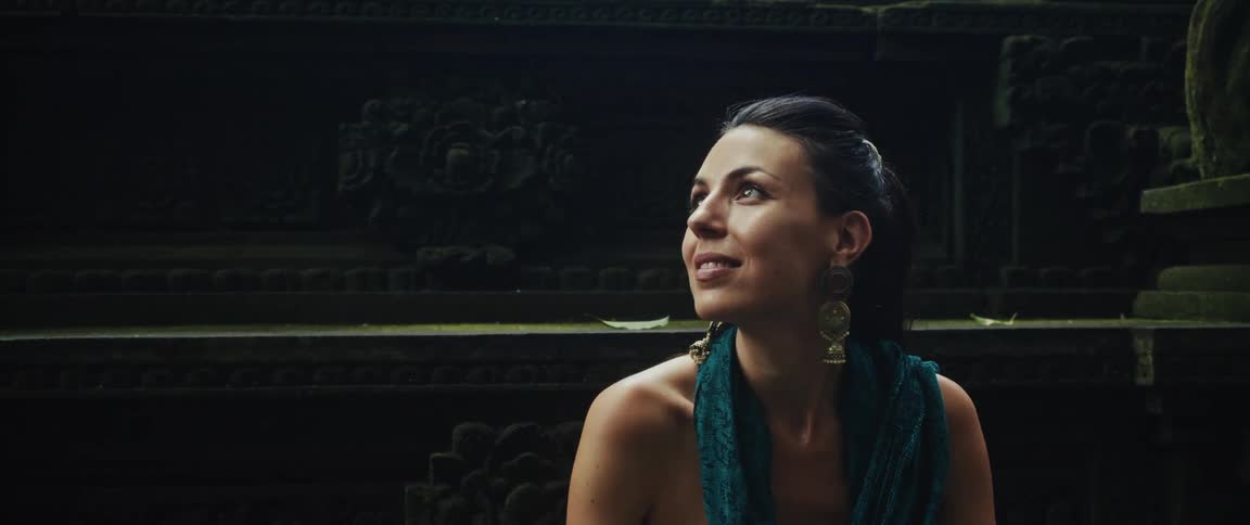A beautiful woman in an ancient moss-covered temple smiles as she looks up in wonder and awe