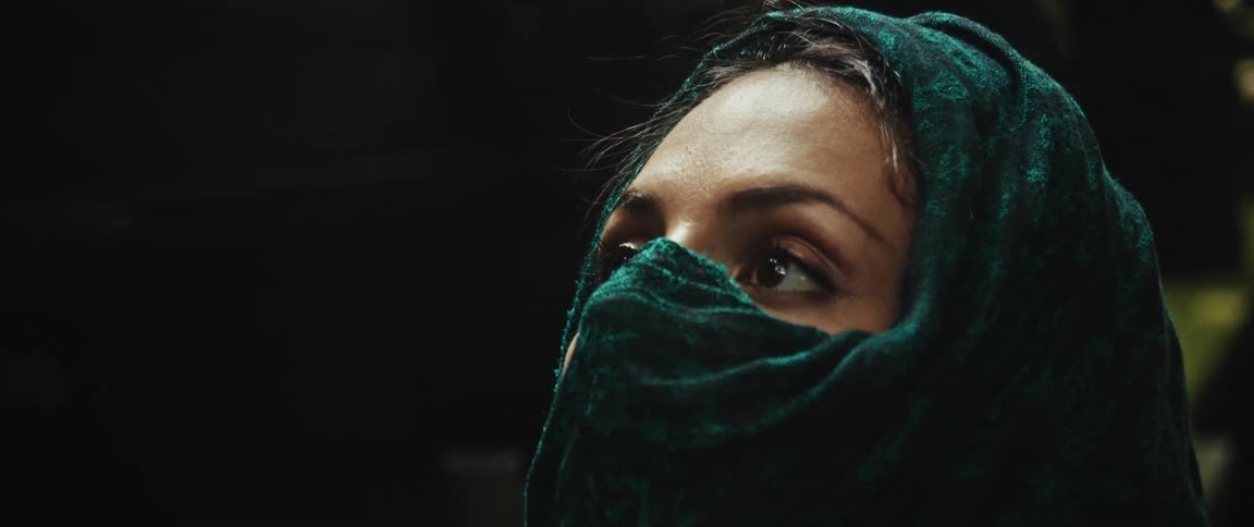 A dramatic close-up on the expressive eyes of a mysterious woman in a green headscarf looking up and then at the camera
