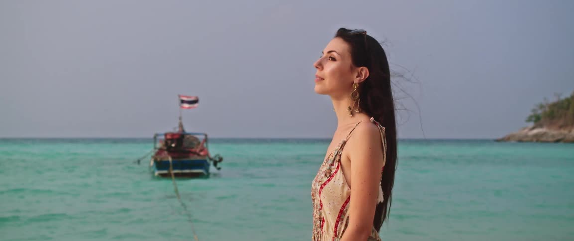A serene woman in a summer dress enjoys the ocean breeze on a beautiful tropical beach in Thailand