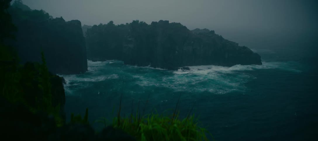 Stormy seas with powerful turquoise waves breaking against black volcanic cliffs on a foggy day