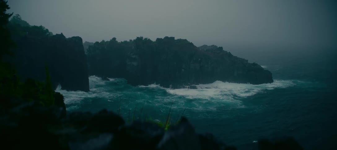 Stormy ocean waves relentlessly crash against rugged cliffs on an overcast and moody day