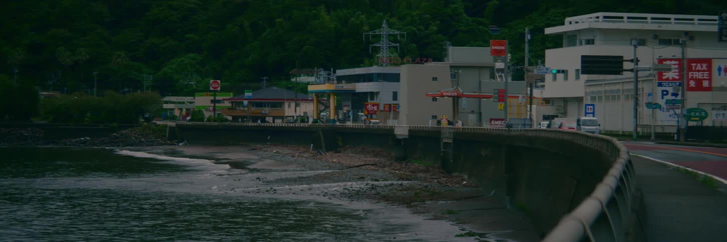 Gentle waves lap the shore of a small Japanese coastal town under an overcast sky
