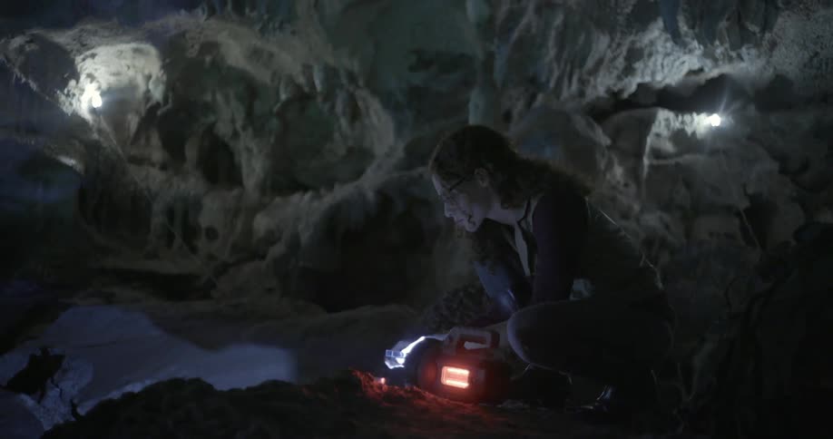 A woman sits next to a blinking light in a cave