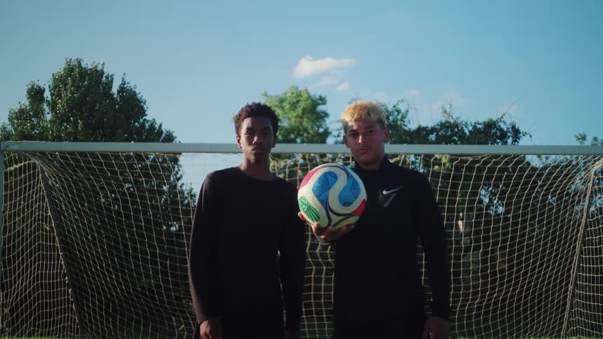 Portrait of two determined young male soccer players standing with a ball in front of the goal on a sunny day