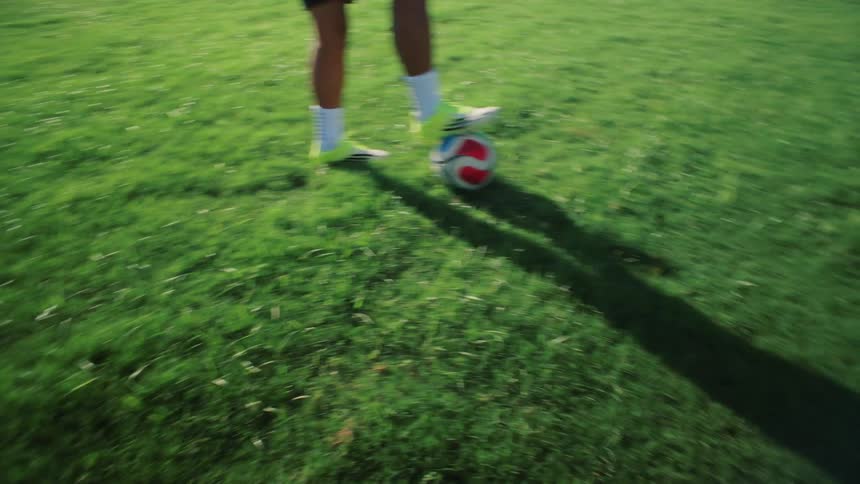 Close up of a soccer player's cleats stopping a rolling ball on a sunny grass field