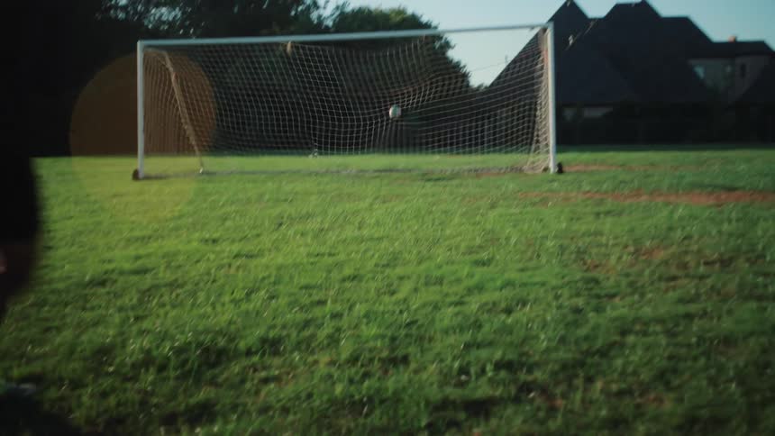 Slow motion shot of a soccer player kicking a ball and scoring a goal on a green field during a sunny day