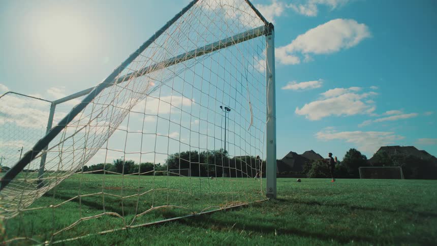 A wide-angle, low-shot view from behind a soccer goal as kids practice on a sunny day with a blue sky