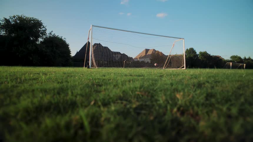 Low angle slow motion shot of an athlete dribbling a soccer ball and scoring a goal on a bright sunny day
