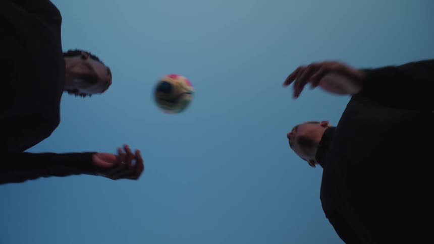 A slow motion, low angle view of two silhouetted young men heading a soccer ball back and forth against a clear blue sky
