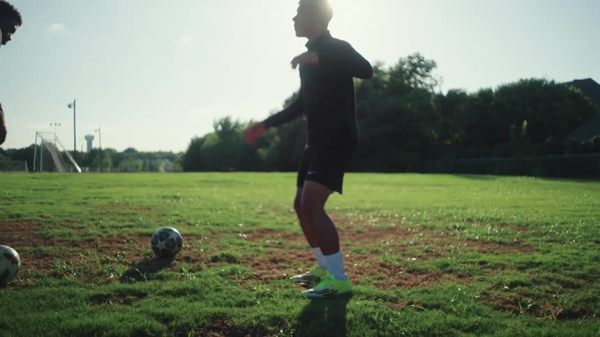 A skilled soccer player practices freestyle juggling tricks in slow motion on a sunlit field