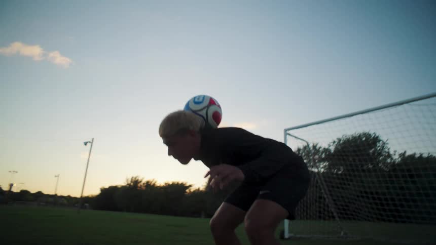 A skilled young soccer player performs an impressive neck stall with a ball on a field at sunset in slow motion