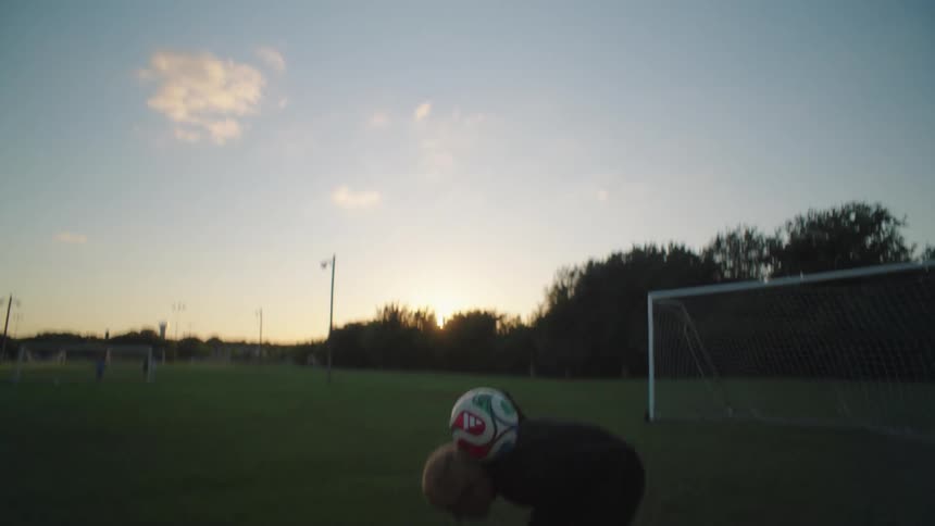 Two skilled soccer players practice juggling and passing the ball back and forth on a field at sunset