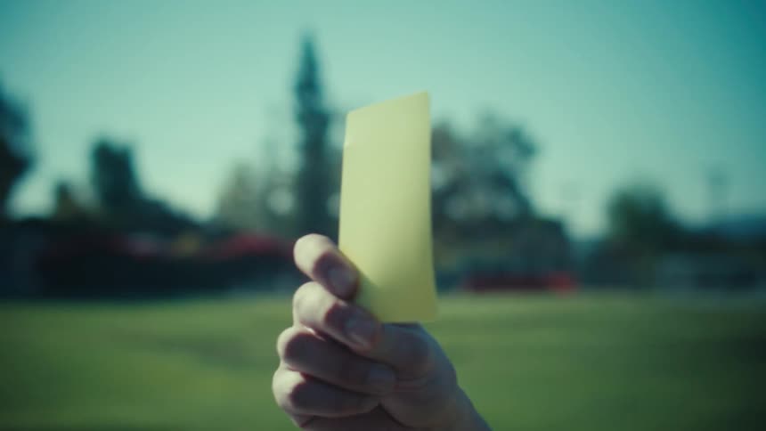 A soccer referee holds up a yellow card in slow motion on a sunny day