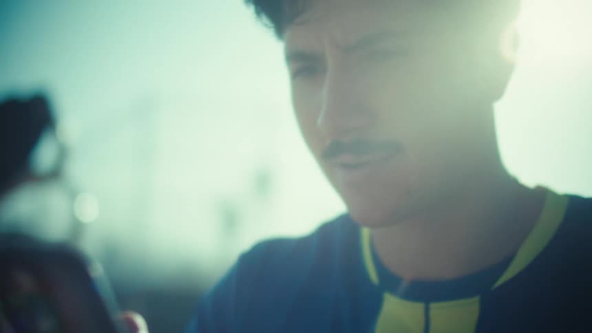 Intense close-up of a focused young man using his smartphone, backlit by a strong, cinematic sun flare