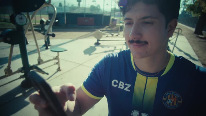Slow motion close up of a young soccer player scrolling on his smartphone at a sunny outdoor park gym
