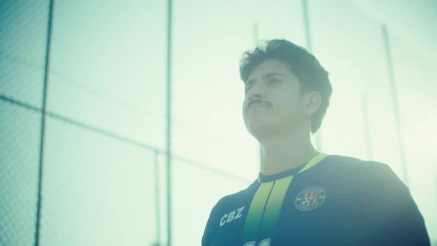 Slow motion reveal of a young soccer captain holding a ball, looking determined in a sunny urban alley before walking away