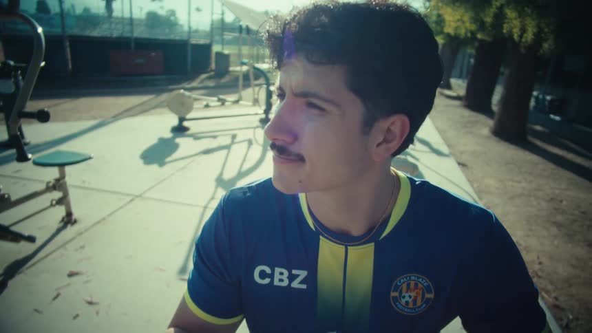 A thoughtful soccer player with a mustache scrolls on his phone while sitting at an outdoor workout park in slow motion