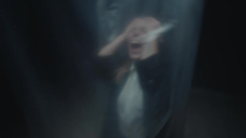 A terrified woman screams in a dark, confined space, seen through a distorted, blurry veil