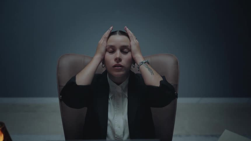 A stressed and overworked businesswoman feels overwhelmed, holding her head in her hands while working late in a dark office
