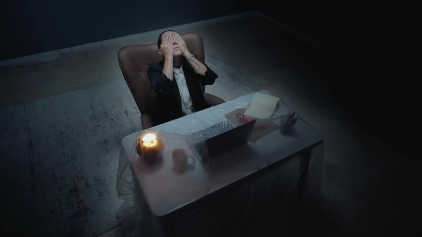 A tired businesswoman working late by candlelight in a dark, isolated office feels the stress of her work