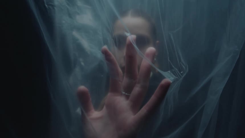 Slow motion shot of a mysterious woman in a suit pressing her hand against a translucent plastic barrier
