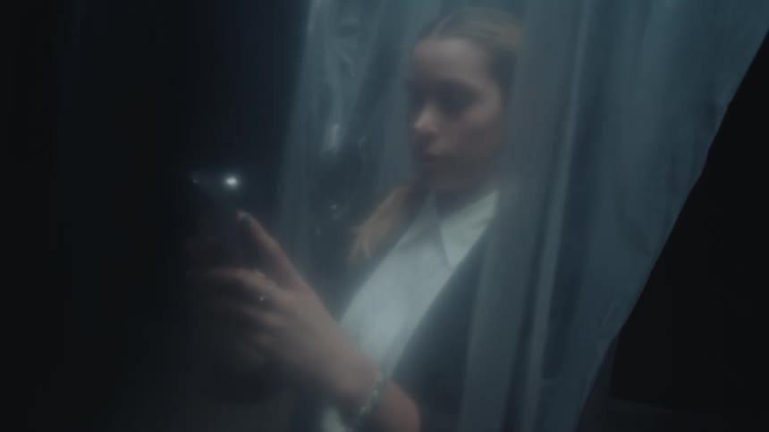 A business woman looks at her phone in a dark room, viewed through a translucent plastic sheet