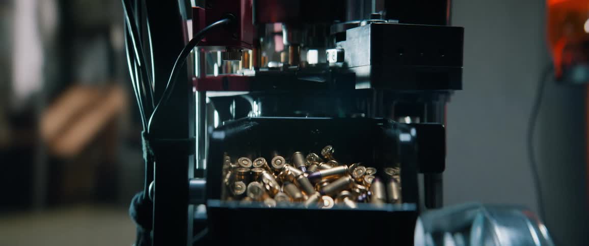Cinematic slow-motion close-up of an ammunition reloading machine assembling bullets and filling a container