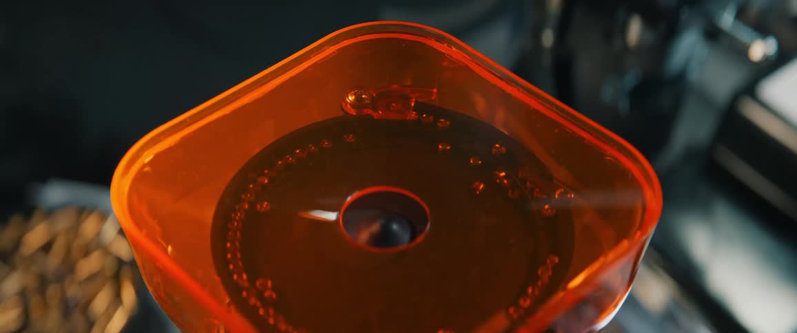 Extreme close-up of whole coffee beans falling into the orange hopper of an electric coffee grinder