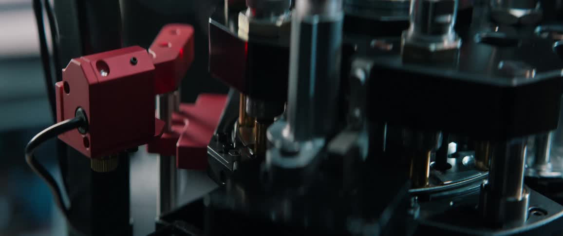A detailed macro shot captures an automated reloading press assembling ammunition on a rotating carousel in a factory