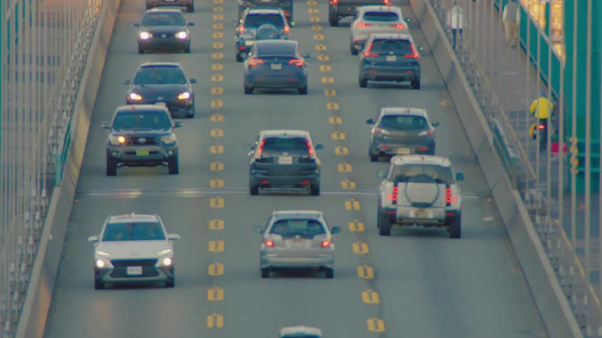 Dynamic zoom reveals heavy traffic commuting across the Lions Gate Bridge with scenic sunlit mountains in the background