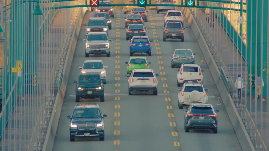 Dramatic zoom-out reveals cars driving over the scenic Lions Gate Bridge with a beautiful mountain range in the background at sunrise
