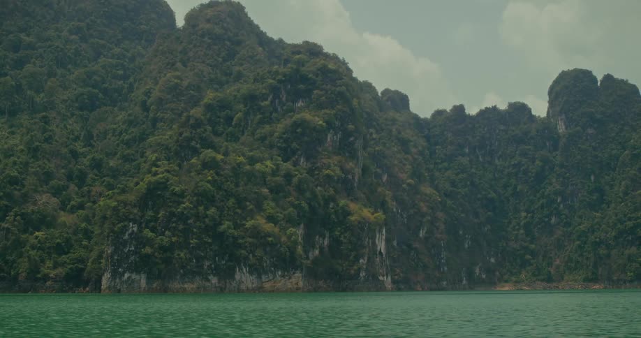 A tranquil view of a vast emerald lake surrounded by majestic, jungle-covered mountains