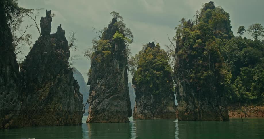 Towering tree-covered limestone pillars emerge from the tranquil green waters of a vast lake