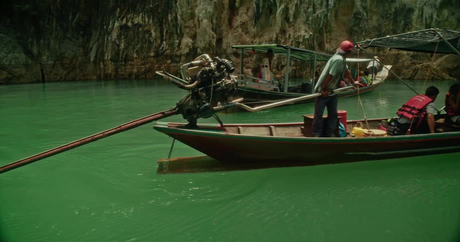 A Thai long-tail boat with tourists glides through the emerald green waters of a lake surrounded by majestic limestone cliffs