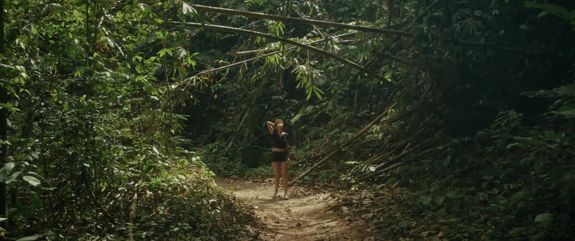 A female explorer with a backpack walks down a dirt path surrounded by a lush bamboo forest