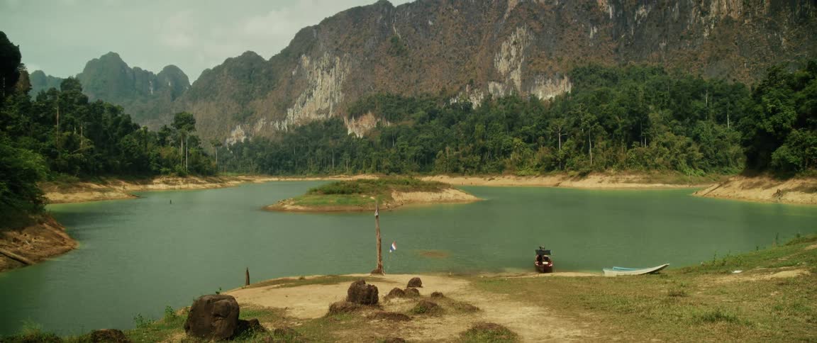 A slow pan across a serene lake in a valley surrounded by majestic limestone cliffs and lush jungle