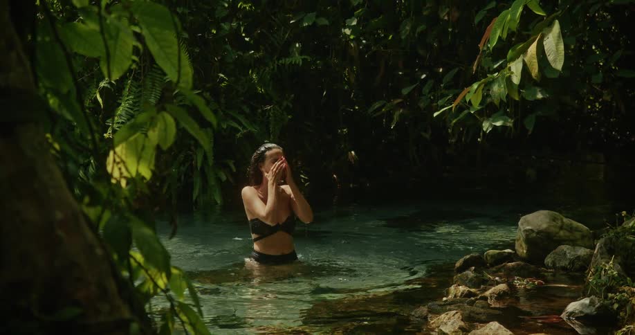 A joyful woman in a bikini laughs and refreshes herself in the clear, cool water of a secluded jungle spring
