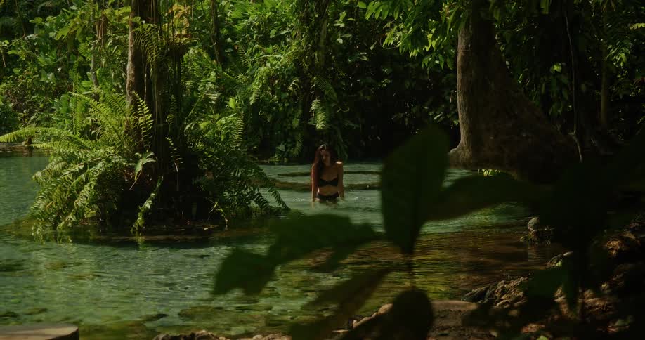 A woman in a bikini soaks in the tranquil beauty of a crystal-clear jungle river before joyfully splashing water into the air