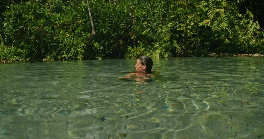 A woman enjoys a serene swim in a crystal-clear jungle river on a sunny day