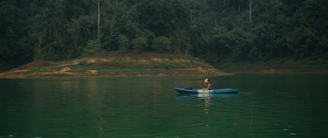 A woman peacefully paddles a kayak across a serene green lake surrounded by a lush forest