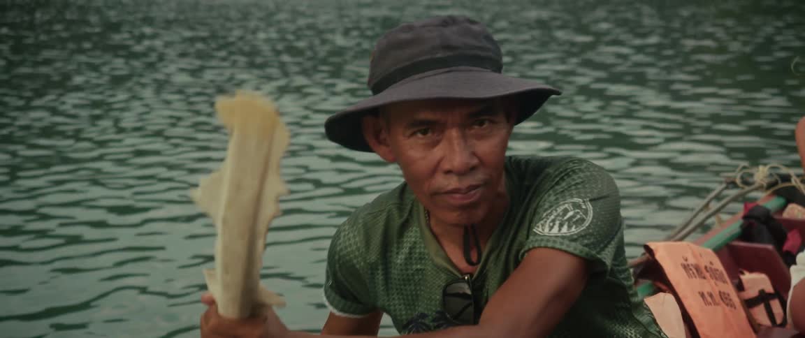 Close-up slow-motion footage of a local guide paddling his canoe and looking directly at the camera on a calm lake