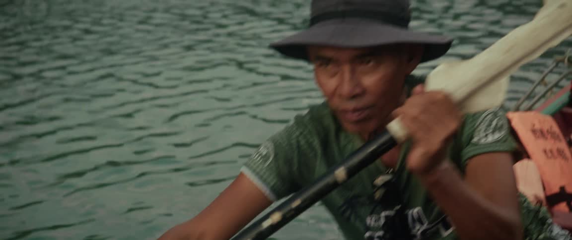 A local guide paddles his boat in slow motion on a calm lake before holding up a sawfish rostrum