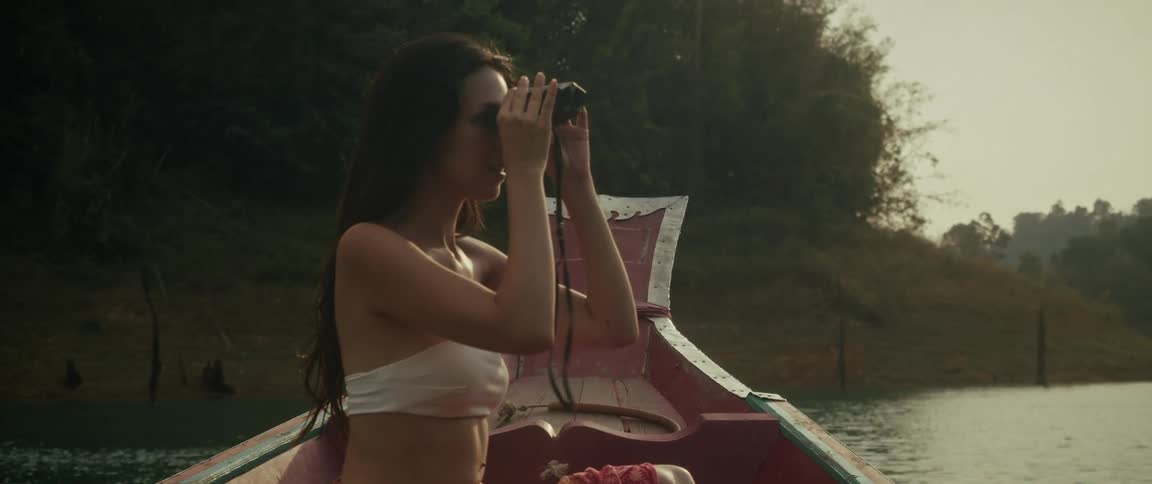 A curious woman enjoys a peaceful boat ride on a jungle lake, smiling as she points out the sights before looking through her binoculars