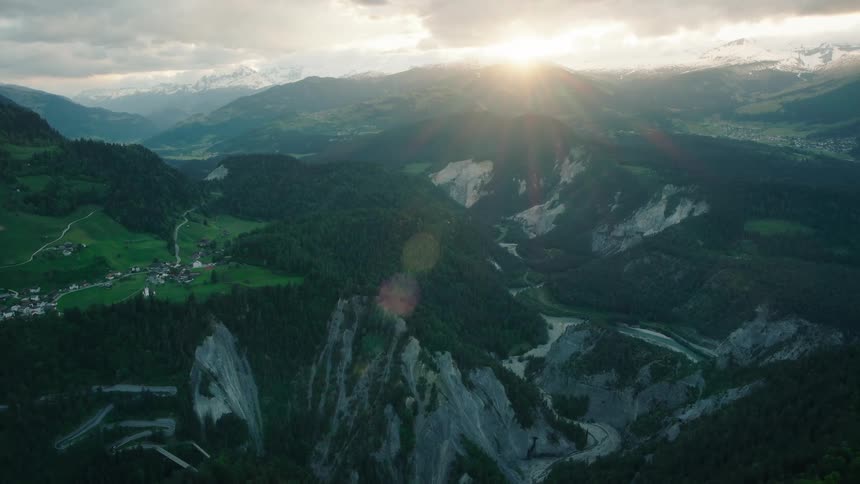 A majestic static aerial shot captures the sun setting over a vast mountain canyon with a river and small village below