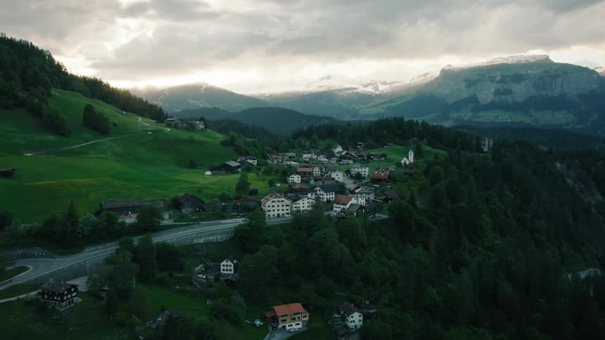 A stunning aerial view shows a picturesque village nestled in the green mountains of the Swiss Alps at sunrise