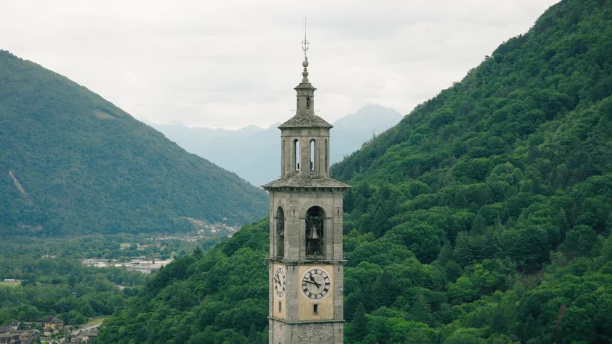 A classic European clock tower stands majestically against lush green mountains in a picturesque timelapse