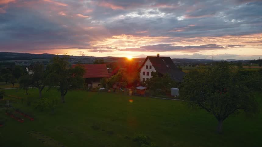 A gentle push-in shot of a quaint European farmhouse nestled in the lush countryside during a breathtaking golden hour sunset