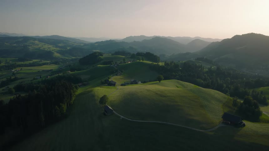 An idyllic aerial view shows the rolling green hills and farms of the Swiss countryside during a beautiful sunrise